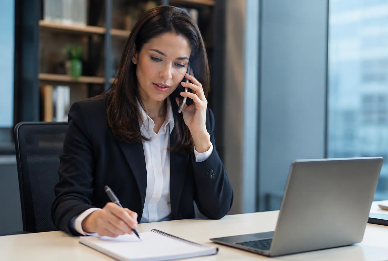 Acquisition advisor answering a business owner's questions by phone at an office desk.